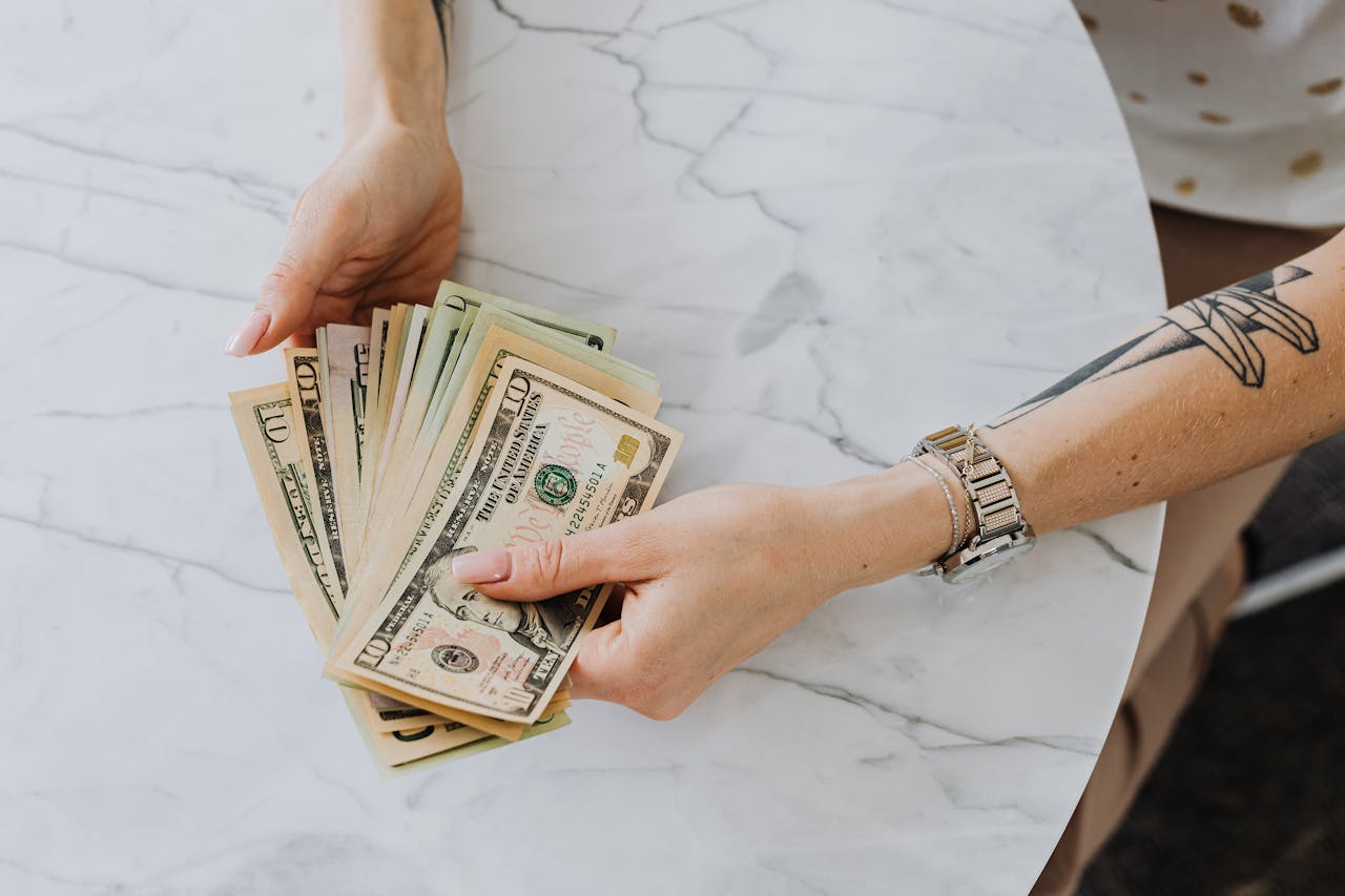 Hands holding and counting US dollar bills on a marble table, depicting wealth and finance.